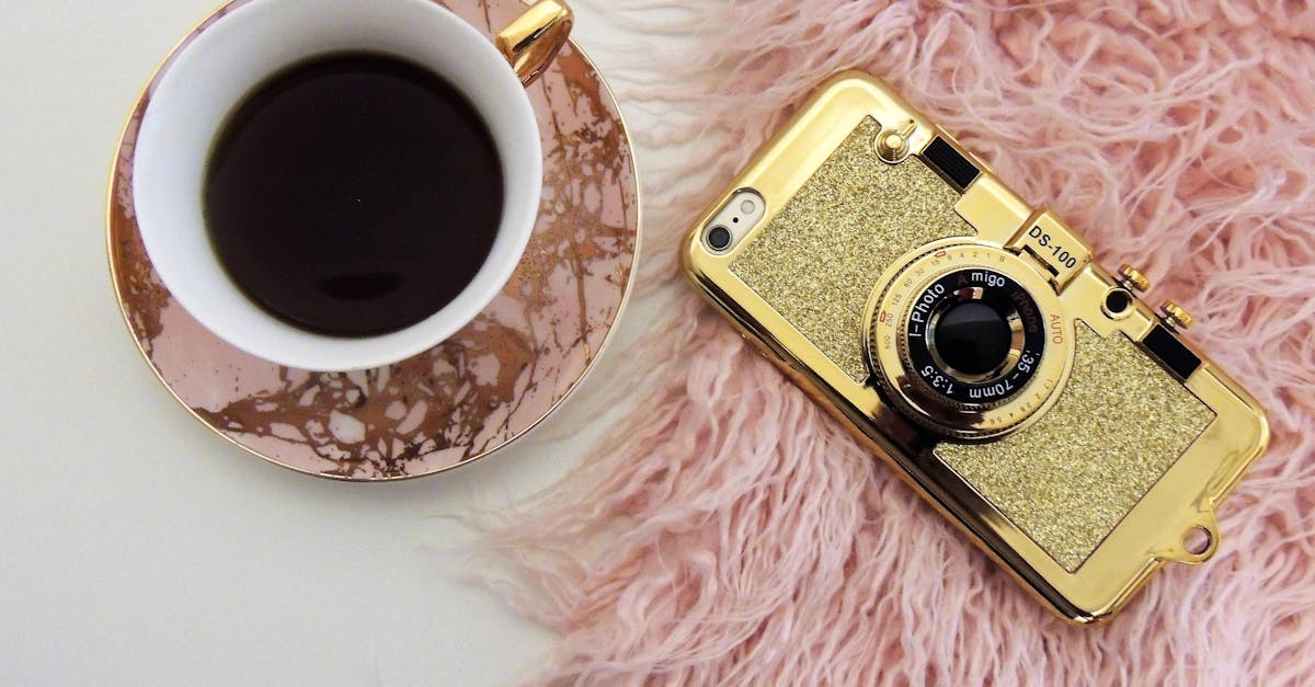 stylish flat lay of a coffee cup and gold camera themed smartphone on a pink fur surface